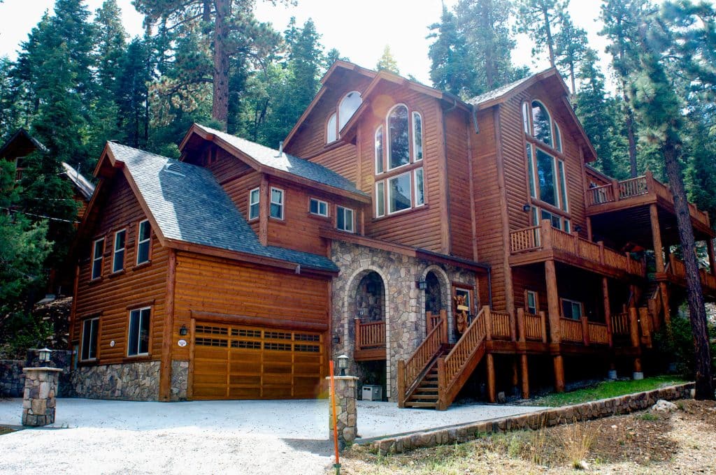 Three-story hybrid log home with stone accents and a two-car garage in a pine forest