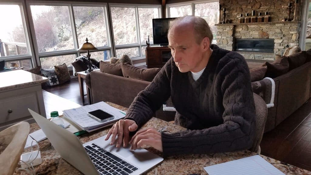 Man working on a laptop inside a hybrid log cabin with a stone fireplace